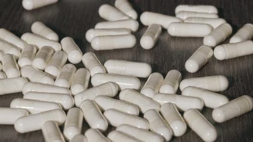 Falling White Capsules on a Dark Table