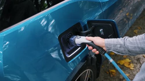 Young man charging electric car outdoor at green forest. Save ecology alternative energy sustainable