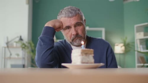A Sad Elderly Man Celebrates the Holiday Alone Blowing Out a Candle on a Cake