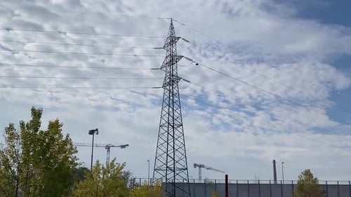 An electricity pylon with power lines and distant industrial elements.