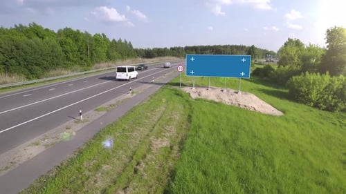 Billboard poster with blue screen and tracking markers on a busy suburban highway.