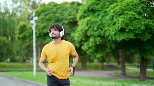 Young adult sportsman runner with headphones jogging in an urban city park. Handsome male