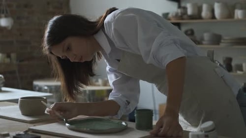 a woman paints a plate with a brush in a pottery workshop