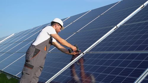Solar Panel Technician with Drill Installing Solar Panels on a Sunny Day