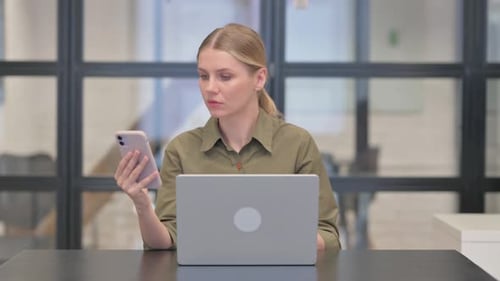 Woman Uses Phone and Laptop in Workplace