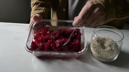 man mixing boiled beets with sesame seeds in glass container in kitchen