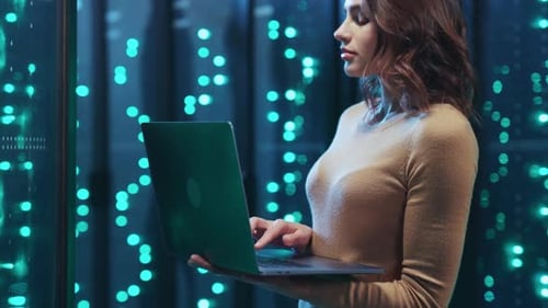 In a Server Room a Woman Confidently Navigates Data on Her Laptop