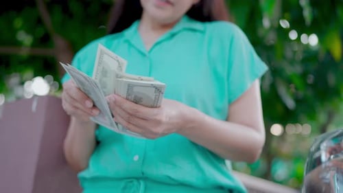 Woman Counting Cash Outdoors in Green Setting