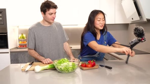 Young couple preparing salad and vlogging in kitchen