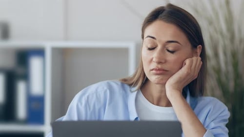 Junge Frau sieht gelangweilt aus, wenn sie in einer modernen Büroumgebung an einem Laptop arbeitet