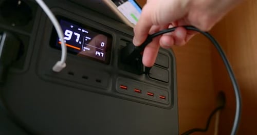 Hand Plugging Black Power Cord Into Portable Power Station With Digital Display For Charging