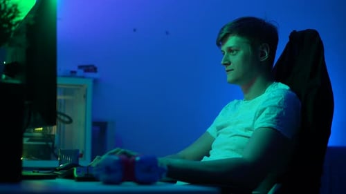 Seitenansicht eines glücklichen Gamer-Mannes, der auf einem Stuhl am Tisch mit modernem Desktop-Computer sitzt