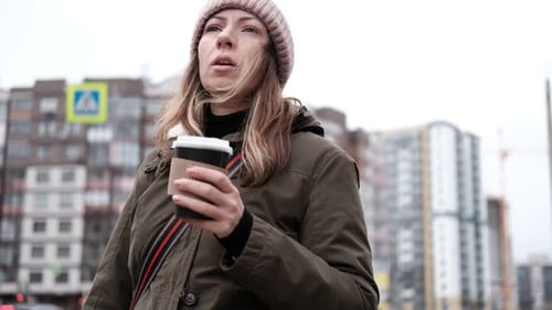 Portrait of Mature Woman in Wool Hat Standing on the Urban Street Drinking Takeaway Coffee From