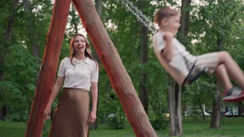 Joyful Park Swing Moment with Mom Supporting Child Under Sunset Light