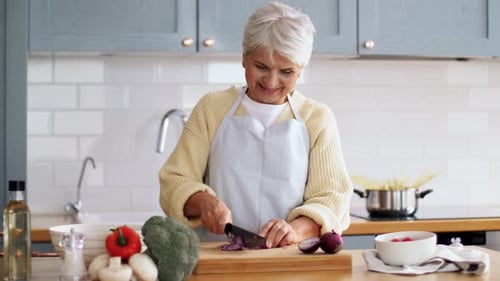 Smiling Senior Woman Chopping Onion in Bright Kitchen