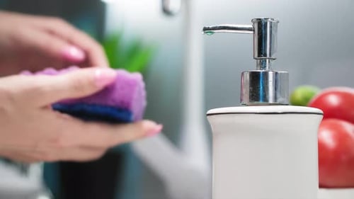 Tareas del hogar: una joven con una esponja en las manos recoge de cerca el detergente para lavar platos