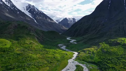 River Flowing Through Green Valley Between Mountains with Snowy Peaks