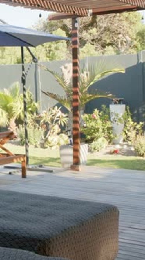 Vertical video: Panning camera revealing woven ottoman on patio under pergola showing garden
