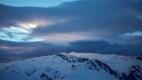 Time lapse shot of dramatic clouds flying over snowy peaks of mountains in winter