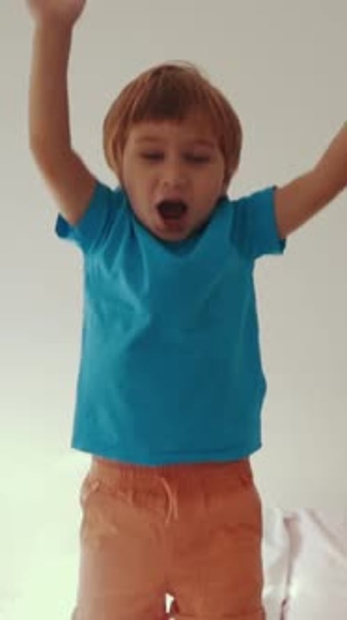 Excited Boy Jumps on Bed in Indoor Setting