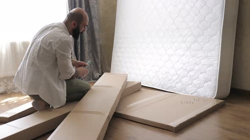 Homme barbu avec le tatouage sur la main déballant la boîte avec les détails du futur lit
