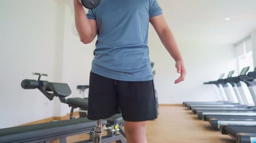 Asian young man with a prosthetic leg lifts a dumbbell at the gym.