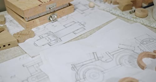 Wooden Details and Draft in Carpentry Workshop From Above of Paper Draft of Toy Car Placed on Table