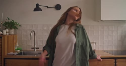 Happy Blonde Girl in a Green Shirt Dancing in the Kitchen at Home