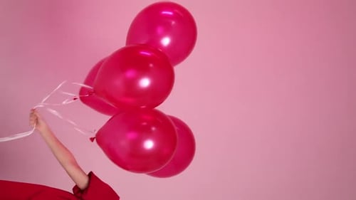 Child Holding Red Balloons Against Pink Background