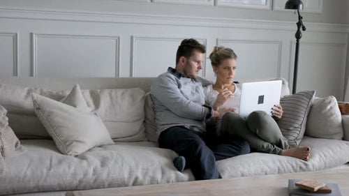Couple relaxing on couch using a laptop