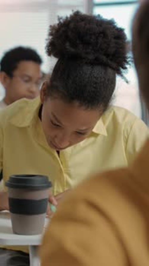 Student Taking Notes in Classroom with Drink