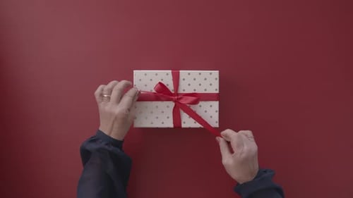 Hands Unwrapping Gift With Red Ribbon on Red