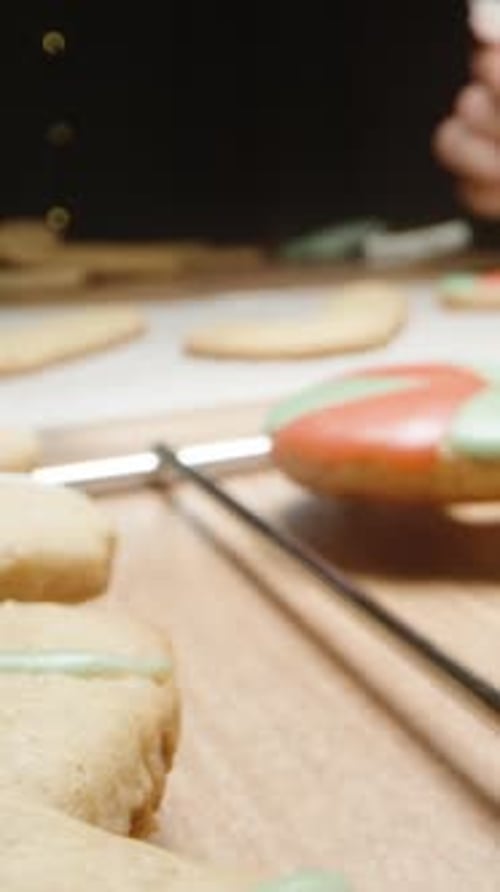 Vertical video. Christmas atmosphere on the kitchen table, a woman decorates gingerbread cookies.