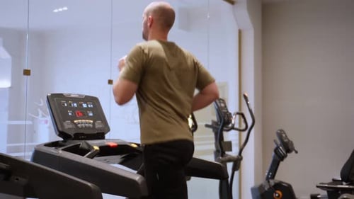 Young Man in Sportswear Running on Treadmill in Front of Window at Gym