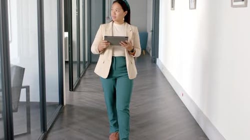 Walking in office hallway, woman holding tablet and smiling confidently