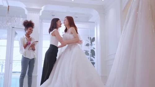 Asian LGBTQ bride trying on wedding gown with her fiance in studio.