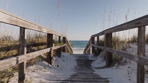 Eye level push in revealing drone shot on wooden walkway leading to empty white sand beach