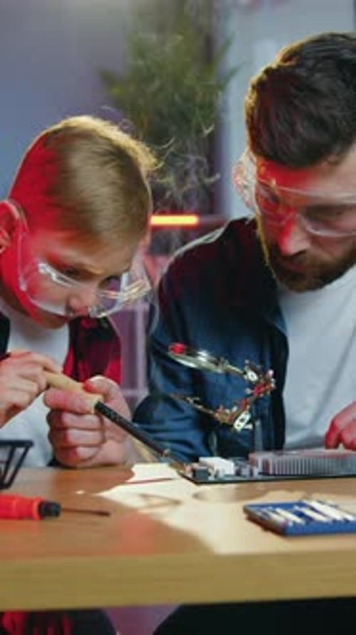 Boy and Man Soldering Electronic Components at Table