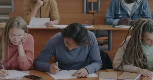 Multiethnic Group of Students Male and Female Writing Examination Tests Sitting at Table in
