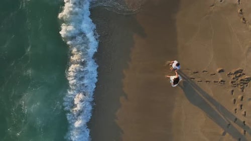 Vista aérea: pareja romántica en la playa viendo la puesta de sol sobre el mar en calma