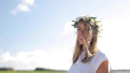 Smiling young woman in flower wreath dances carefree in sunny summer meadow