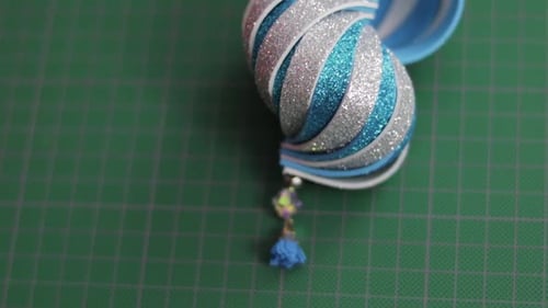 Blue and silver glitter foami christmas ornament on green cutting mat. Tilt.