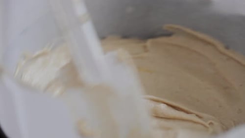 Chef mix cream dough in a metal bowl with plastic spoon while cooking delicious cake at local kitche