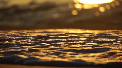 Kleine Meereswelle, verschwommene, weiche, schaumige Wellen, die den goldenen Sandstrand bei Sonnenuntergang waschen