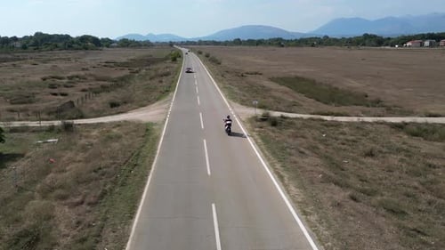 A Drone Flies Behind a Motorcycle Driving Along an Empty Highway