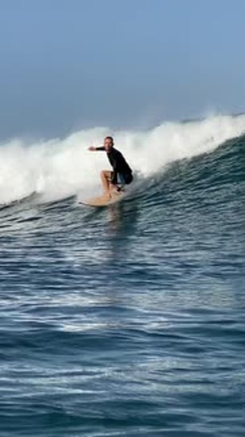Surfer Rides Wave Near Beach on Bright Day