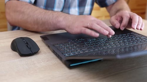 10Close-up of hands using a laptop keyboard and mouse on a wooden desk. Work, internet browsing, and