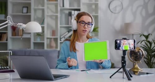 Joven y bonita mujer sentada en el escritorio hace una videollamada, un discurso en una conferencia y muestra una pantalla verde digital