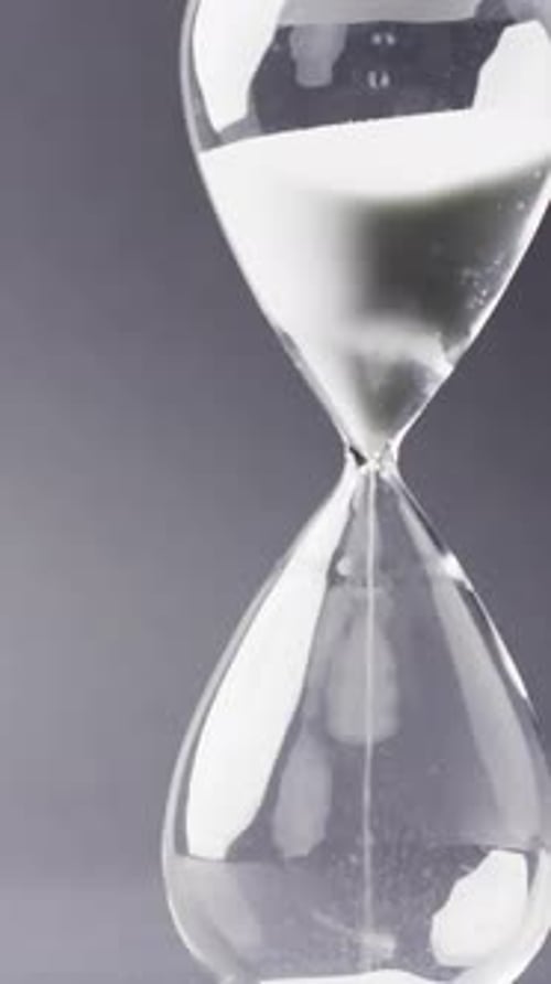 Vertical video of hourglass with sand pouring, copy space on black background