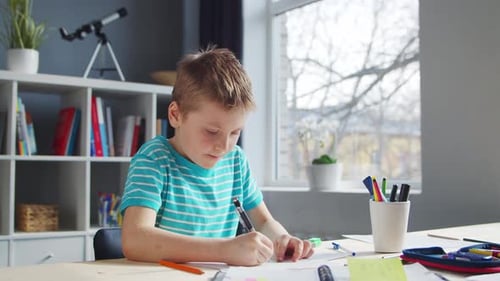 Boy Drawing on Paper at a Table Indoors